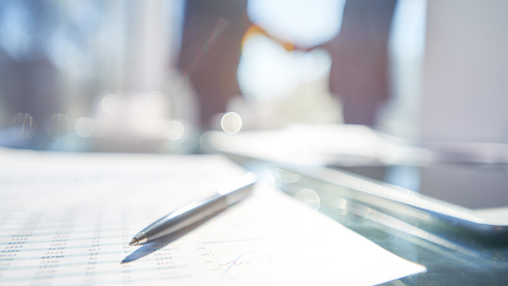 Abstract photo of a pen and paper signifying a contract. Hands shaking in background.