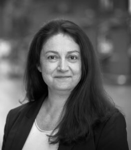 Professional black-and-white headshot of a woman with long dark hair, wearing a blazer for a corporate bio.
